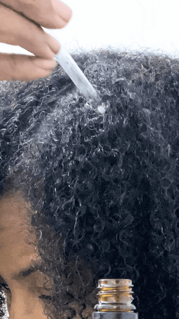 Image of herbal hair oil being applied directly to the scalp with an applicator bottle.