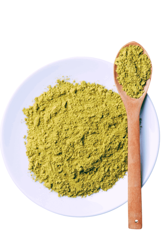 White plate filled with green henna powder and a wooden spoon resting on top, also holding henna.