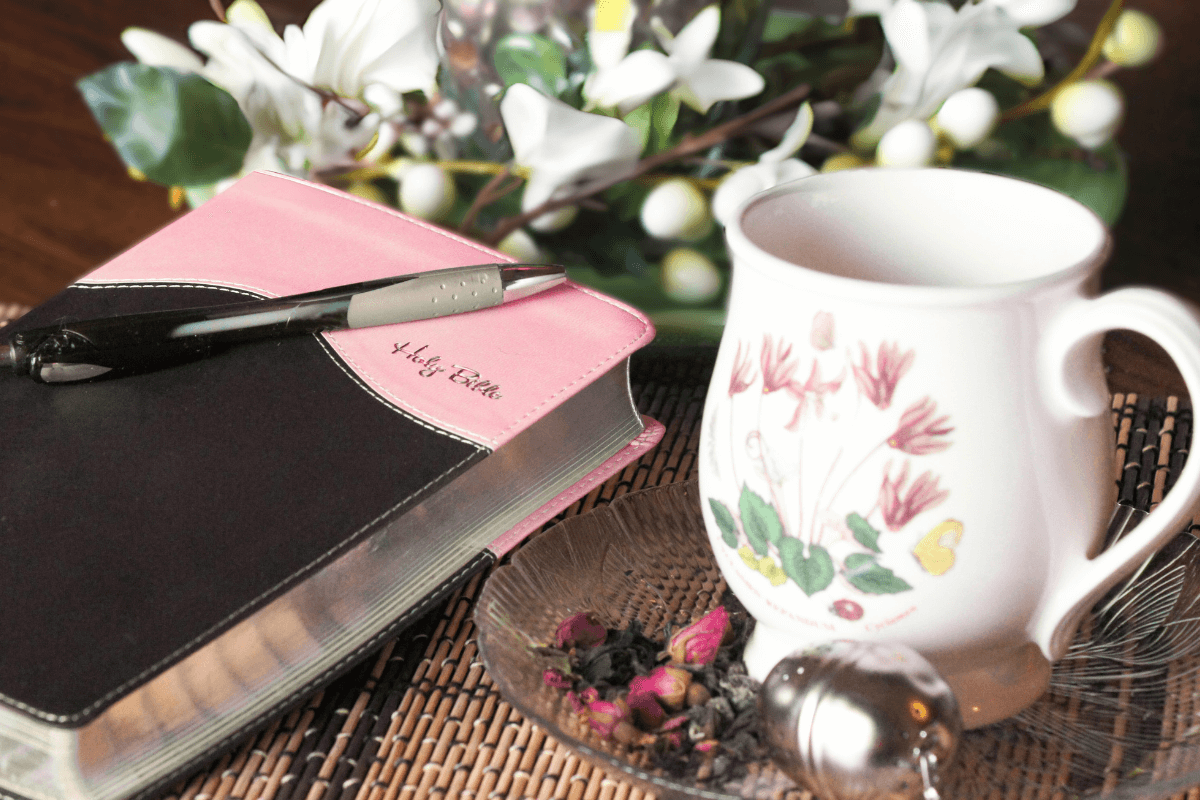 black and pink bible next to some white flowers and a cup of tea