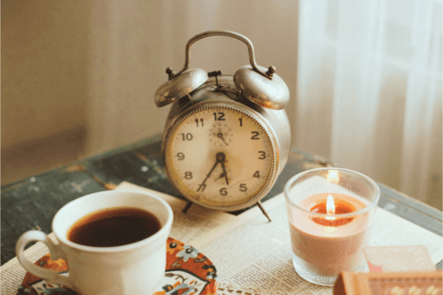 a cup of coffee, clock and a candle on a table in front of the window at the start of a Christian morning routine